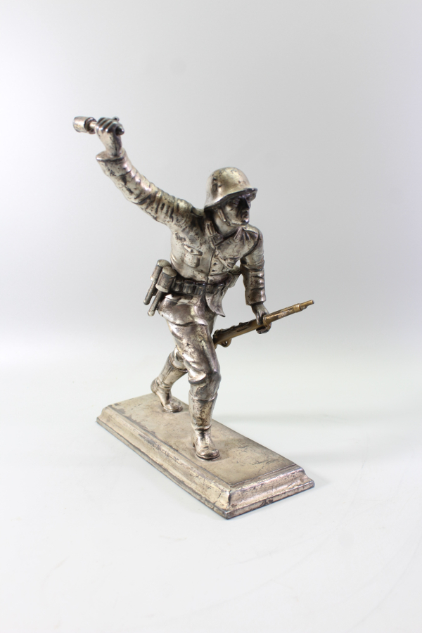 A sculpted figure of an infantryman charging forward with a hand grenade. Silver-plated die-cast metal; total height 23.5 cm.